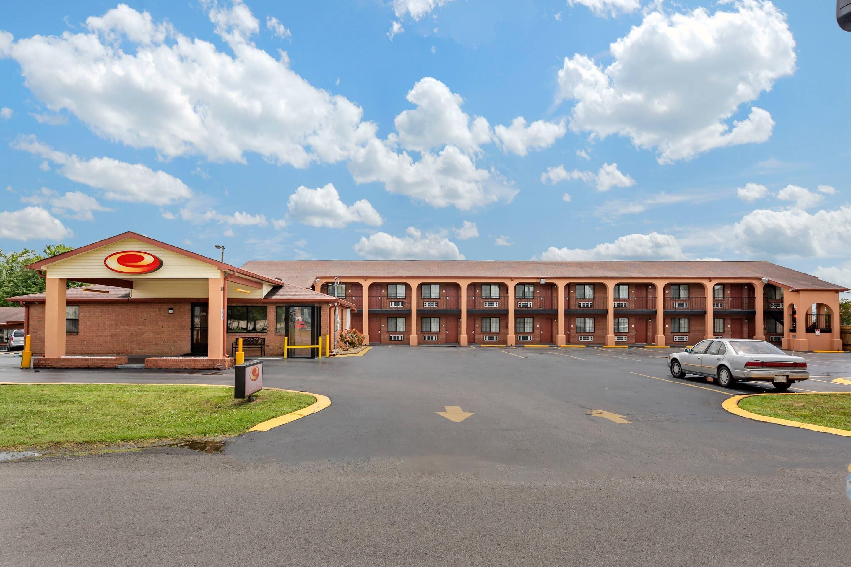 A motel with a central parking area, a drive-through, and a building with a red roof and multiple windows.
