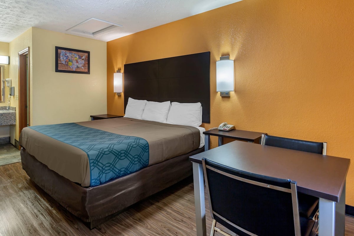 Ein Hotelzimmer mit Bett, Nachttisch, Stuhl und einem an der Wand montierten Telefon.