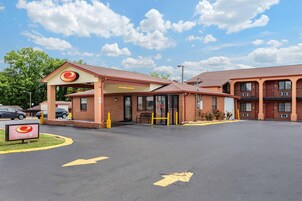 Un motel con entrada cubierta, un estacionamiento con flechas direccionales y un letrero que indica la entrada.