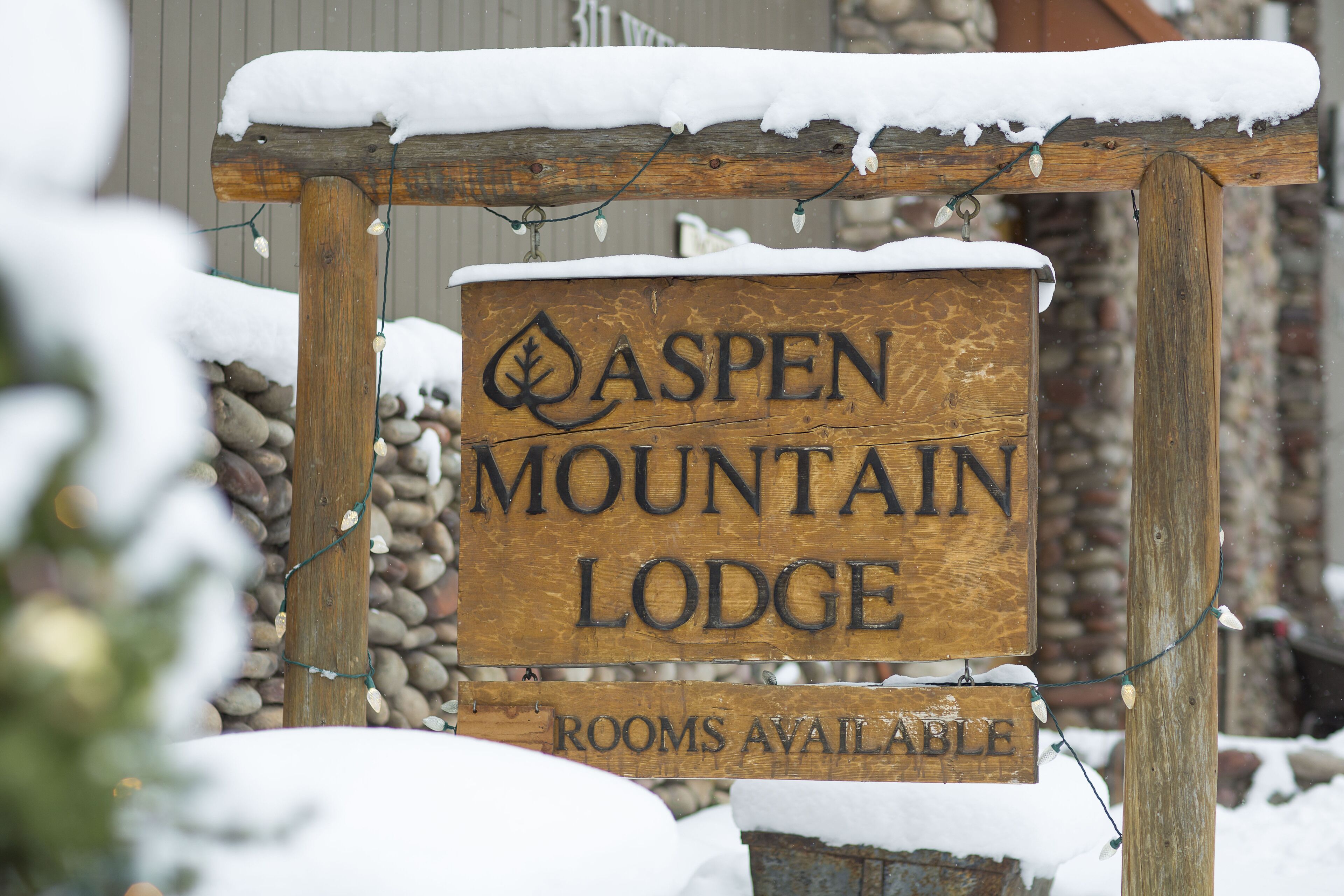 A wooden sign for Aspen Mountain Lodge with a snow-covered top and a message indicating rooms are available.