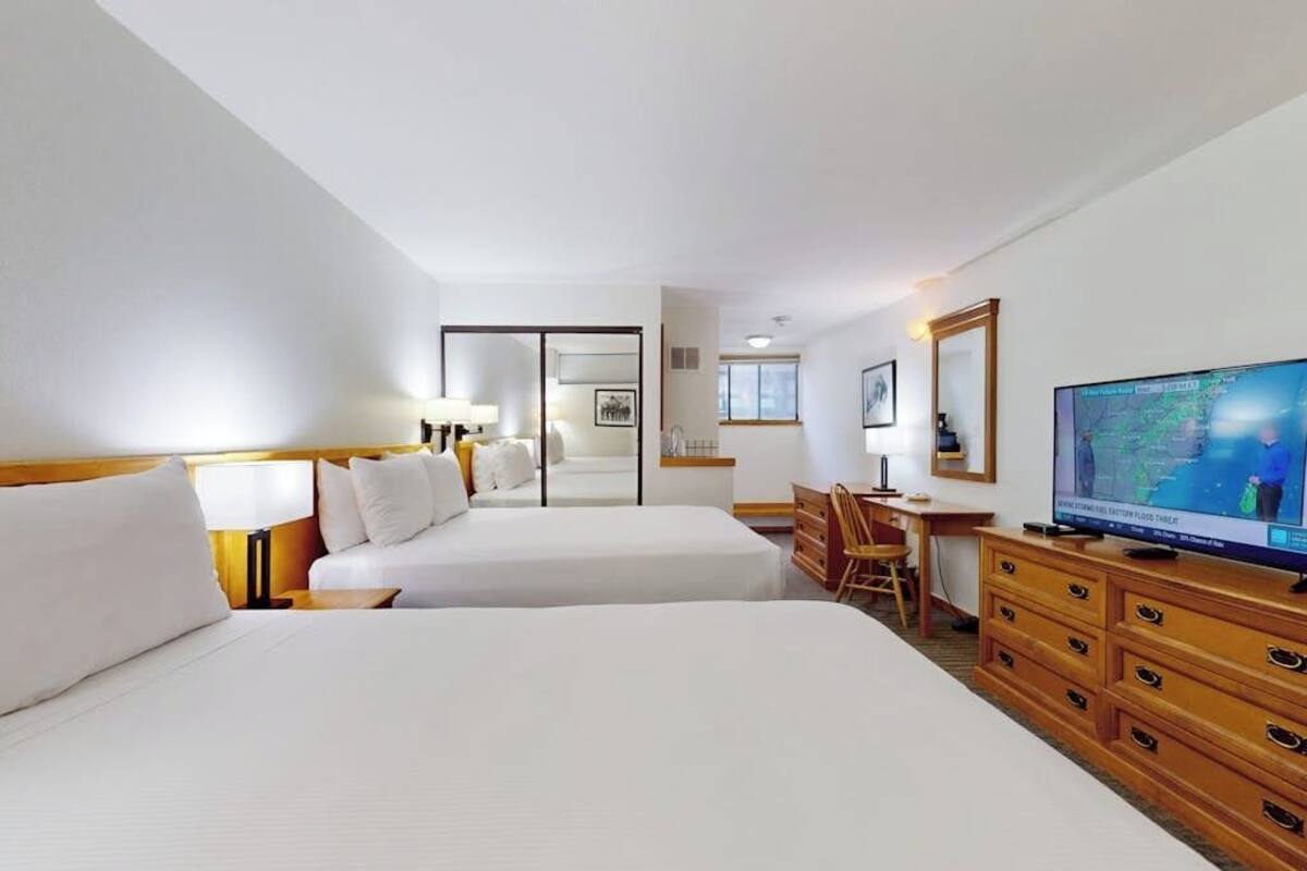 A hotel room with two beds, a desk, a chair, a television, and a dresser.