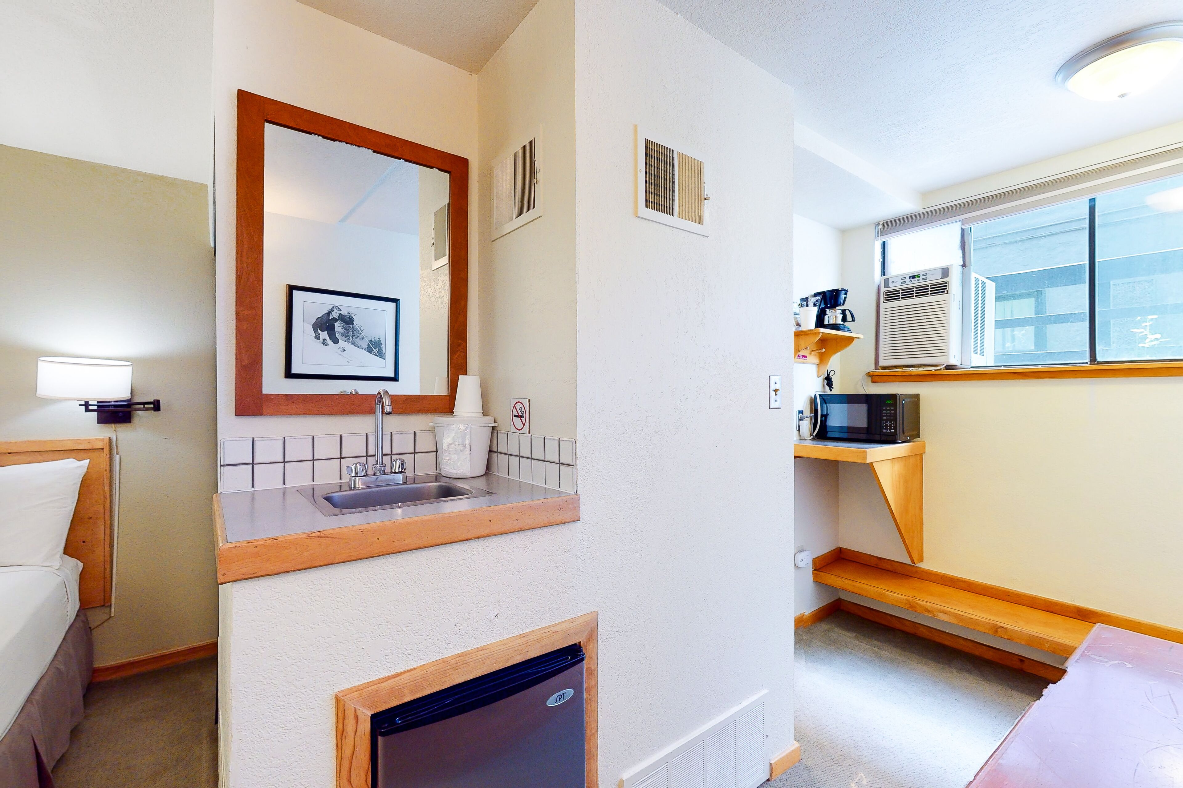 A compact hotel room with a kitchenette, a sink, a microwave, and a refrigerator.
