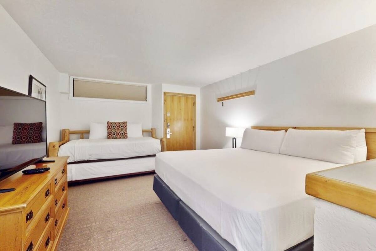 A hotel room with two beds, a wooden dresser, a TV, and a door.