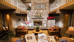 A lobby with a stone fireplace, two leather sofas, a coffee table, and a fireplace mantle with decorations. - Aspen Mountain Lodge (Aspen)