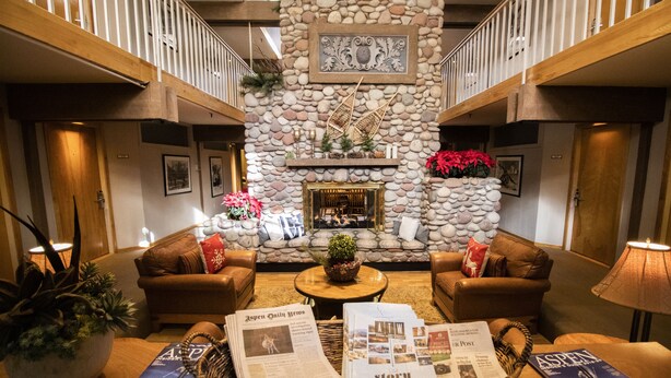 A lobby with a stone fireplace, two leather sofas, a coffee table, and a fireplace mantle with decorations. - Aspen Mountain Lodge (Aspen)