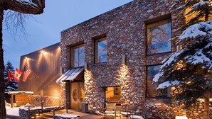 A stone building with a wooden facade, a staircase leading to the entrance, and outdoor seating area. - Aspen Mountain Lodge (Aspen)