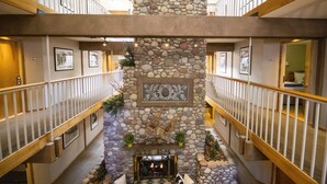 A multi-level hotel lobby with a stone fireplace, wooden railings, and framed artwork on the walls. - Aspen Mountain Lodge (Aspen)