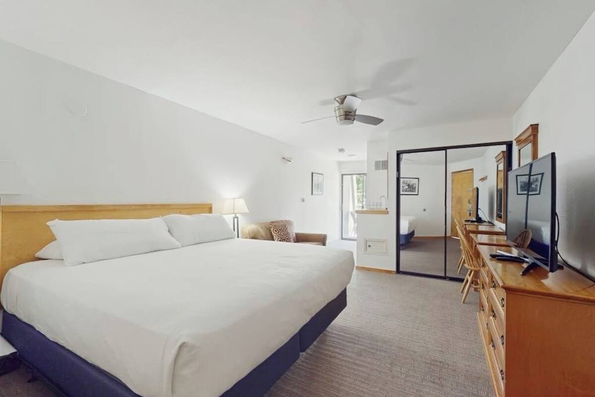 A hotel room with a bed, a desk with a computer, a TV, a ceiling fan, and a mirror.