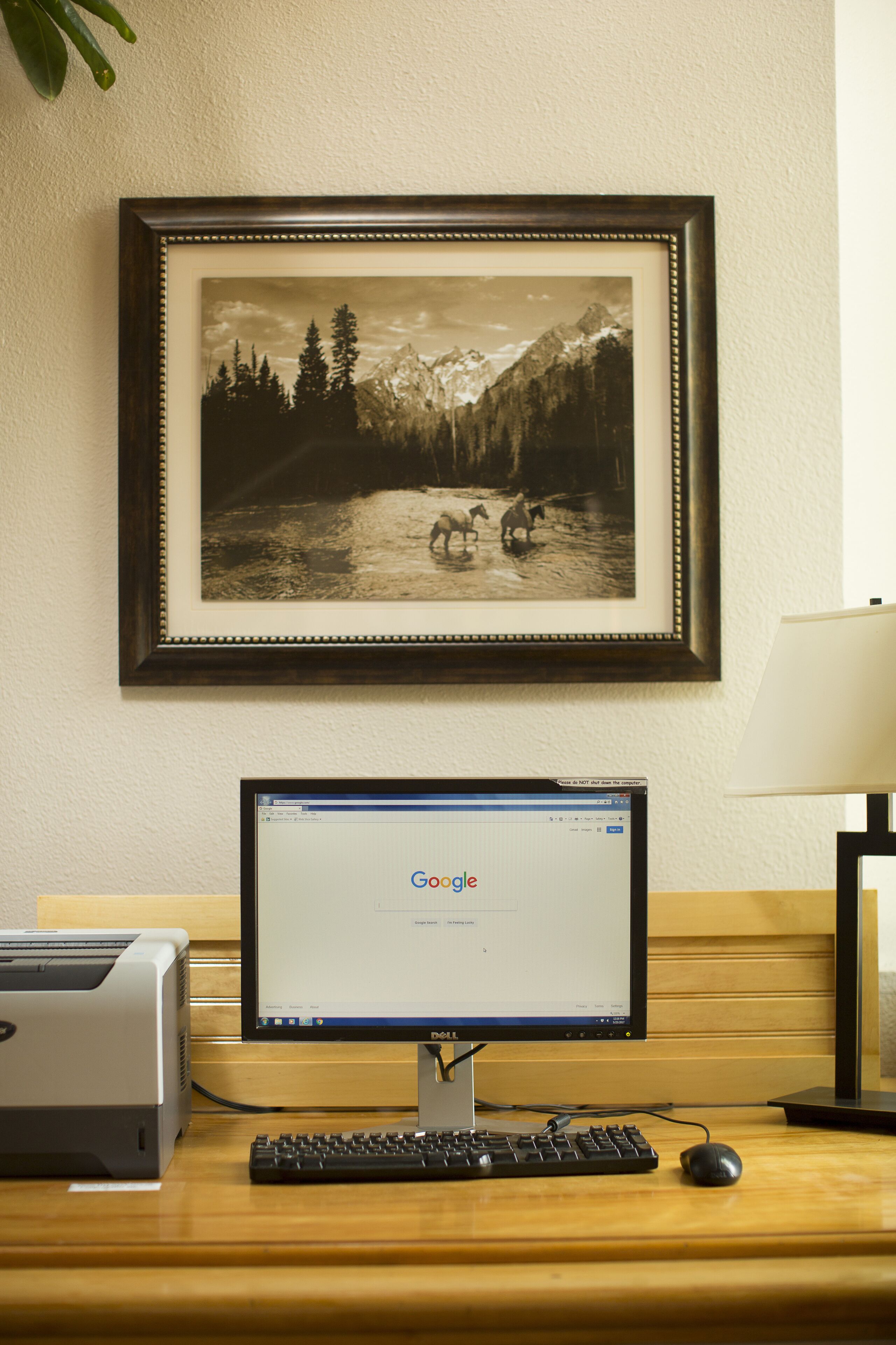 Un ordinateur de bureau, avec une photographie en noir et blanc encadrée représentant un paysage montagneux accrochée au mur derrière.