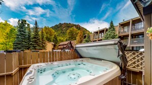A hot tub in an outdoor setting with a wooden fence, a mountain in the background, and a building with balconies. - Aspen Mountain Lodge (Aspen)
