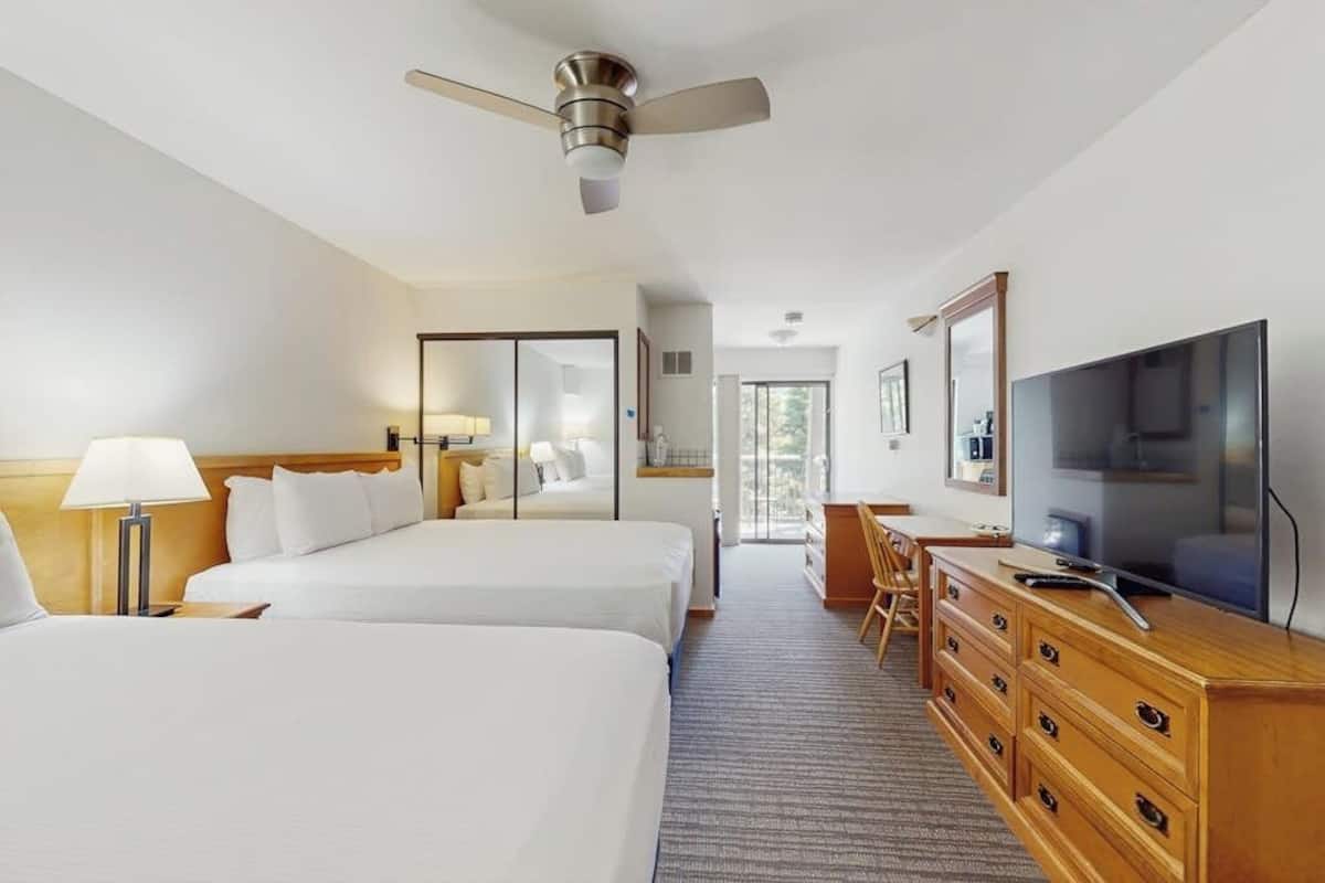 A hotel room with two beds, a desk, a television, and a ceiling fan.