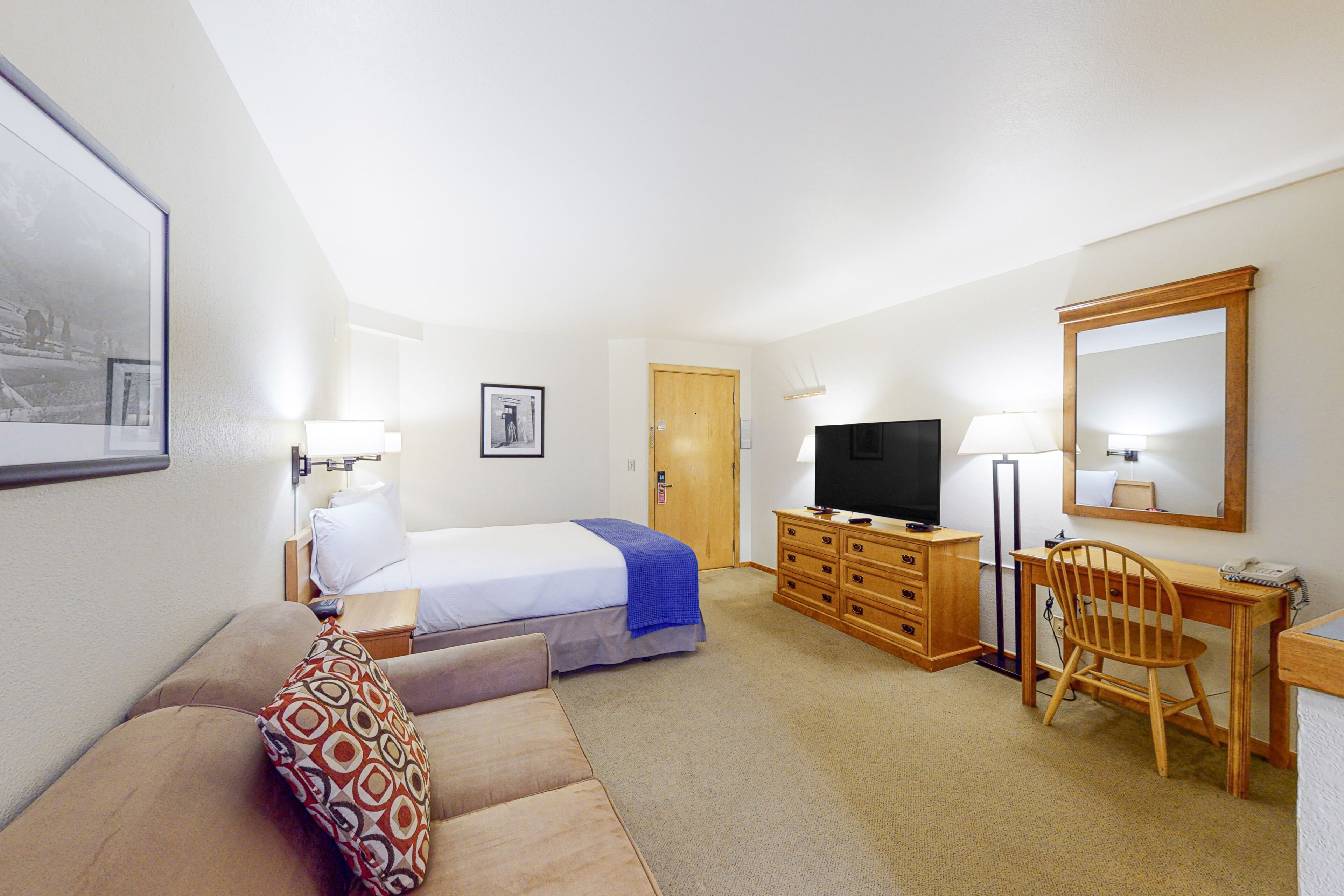 Een hotelkamer met een bed, een bureau, een stoel, een televisie en een spiegel.