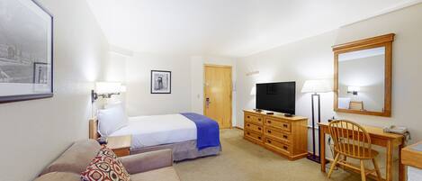 Een hotelkamer met een bed, een bureau, een stoel, een televisie en een spiegel.
