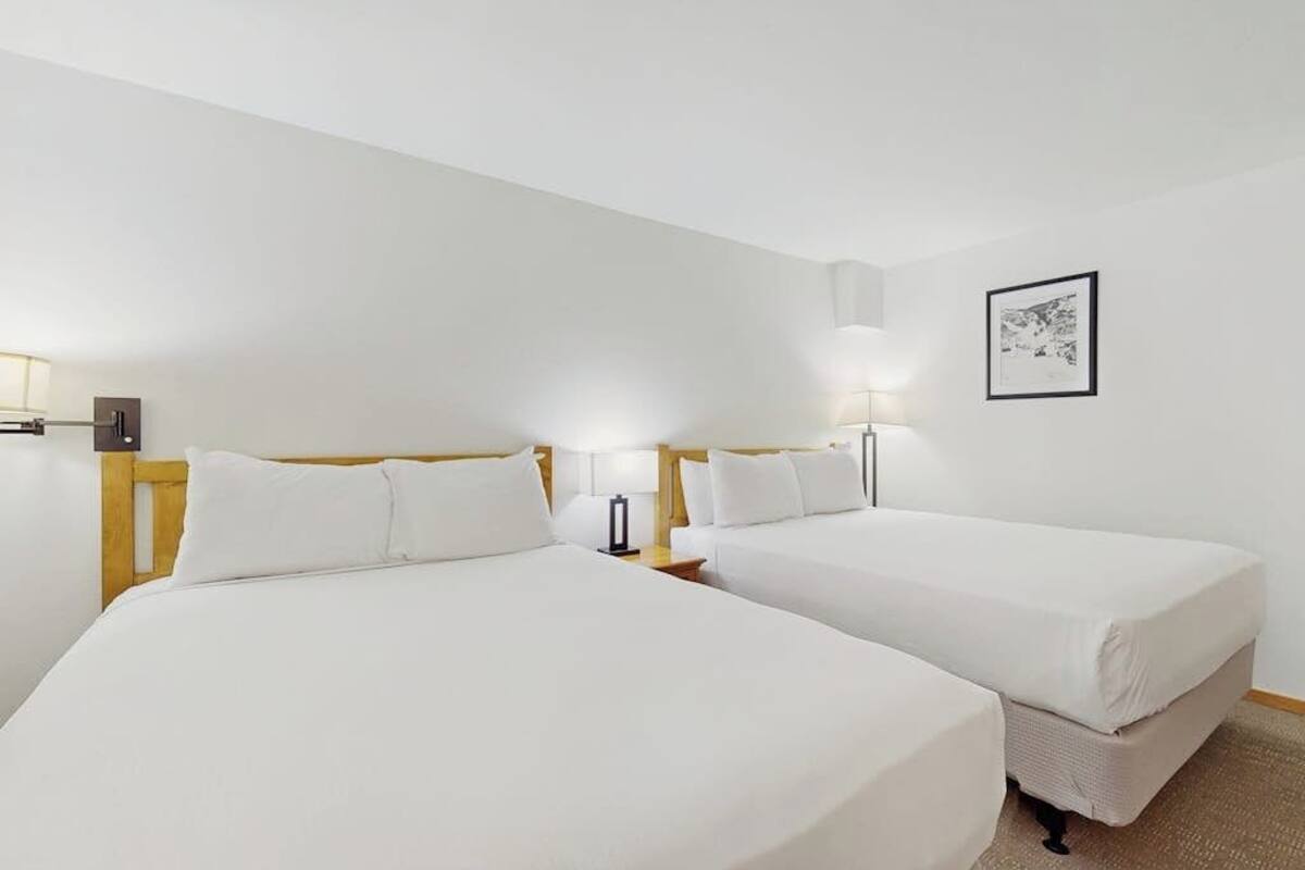 A hotel room with two beds, a nightstand, a lamp, and a framed picture on the wall.