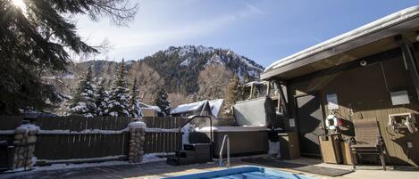 A backyard with a swimming pool, a hot tub, and a covered patio area.
