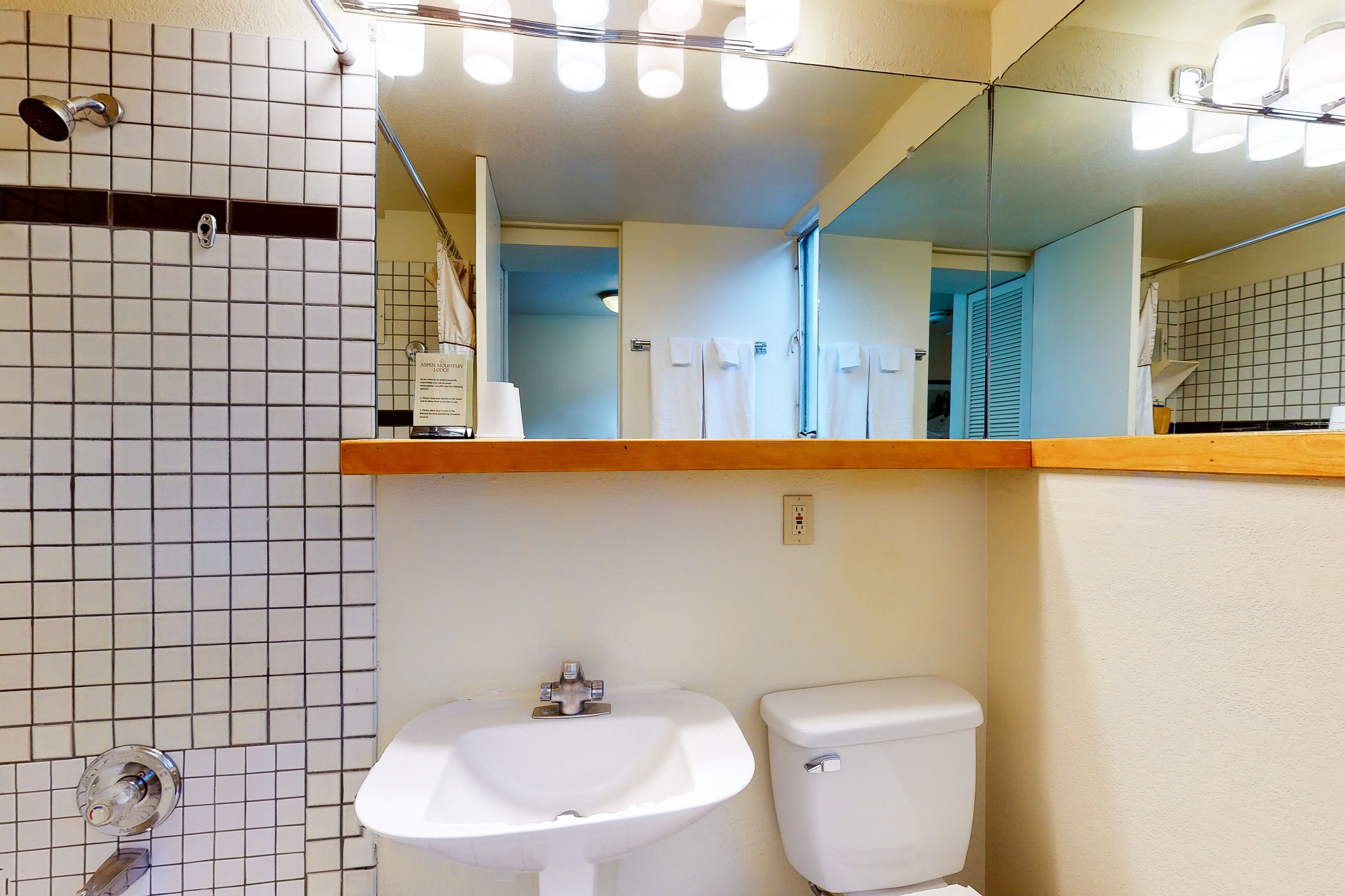 A bathroom with a white sink, a toilet, and a shower. There is a mirror above the sink and a light fixture above the mirror.