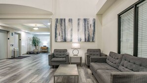 Un salon moderne avec un canapé d’angle gris, deux fauteuils, une table basse et des œuvres d’art abstraites accrochées au mur.