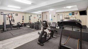Une salle de sport équipée de machines d’exercice, dotée d’un mur avec des miroirs et d’un tapis de course.