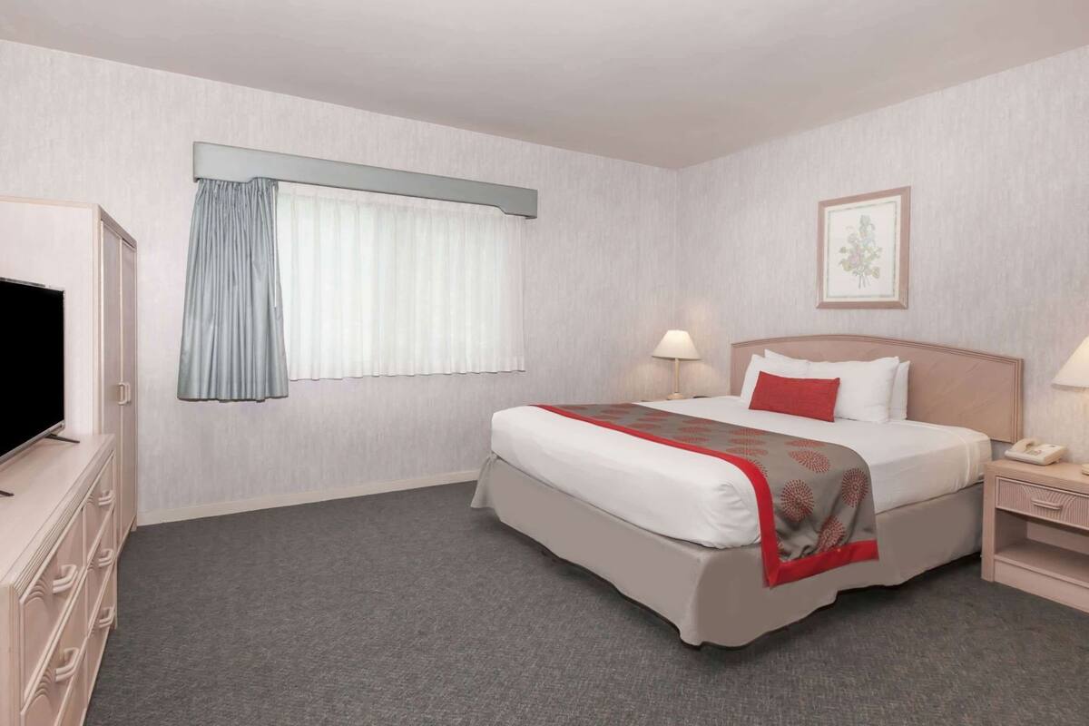 Ein Hotelzimmer mit Bett, Nachttisch, Lampe und Fernseher auf einer Kommode.