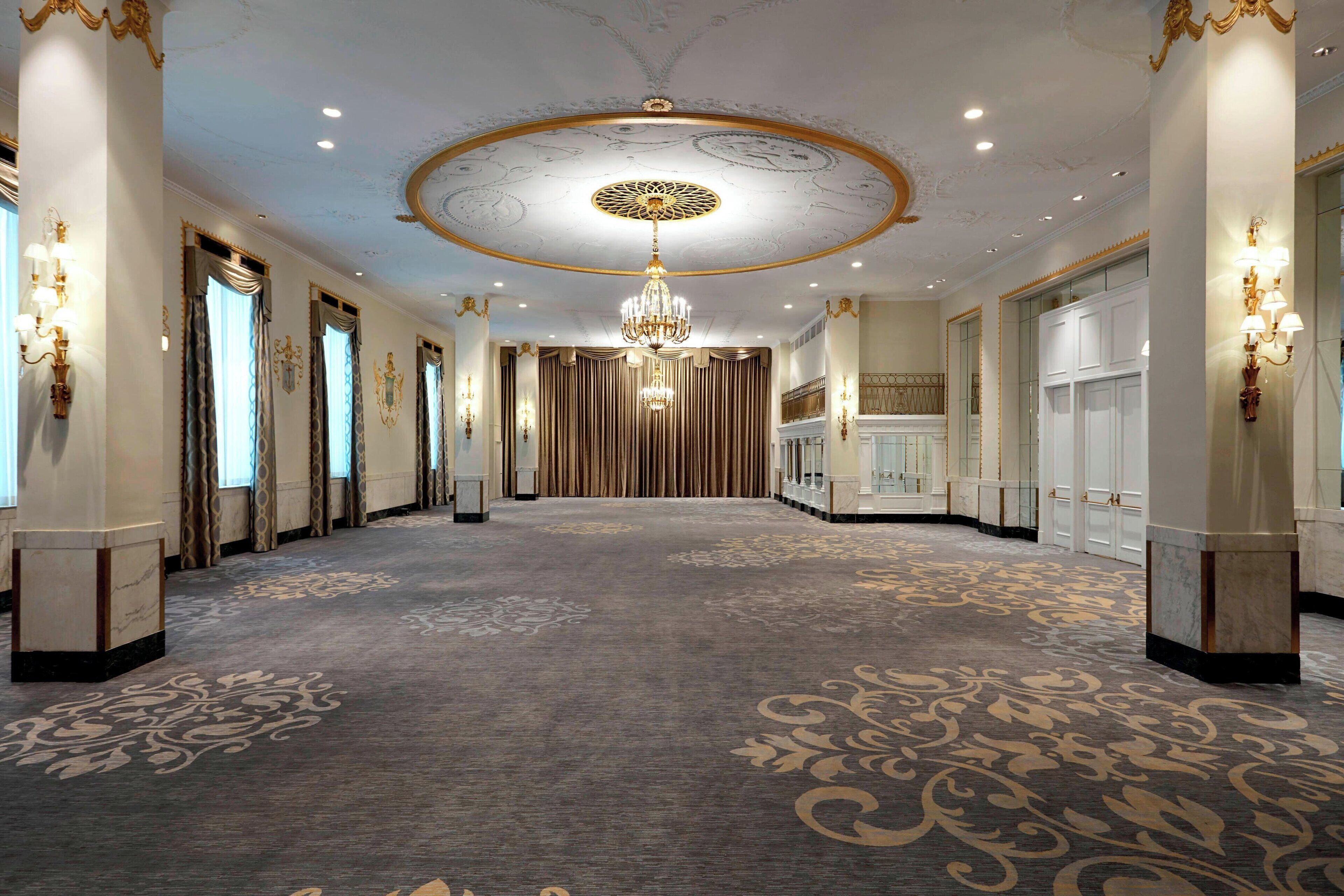 A grand hallway with ornate ceiling, chandeliers, and patterned carpet.