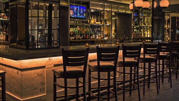 Eine Bar mit Fernseher, Barhocker und Flaschenregalen.