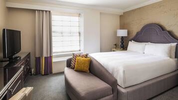 A hotel room with a large bed, a TV, a desk, and a window with curtains.