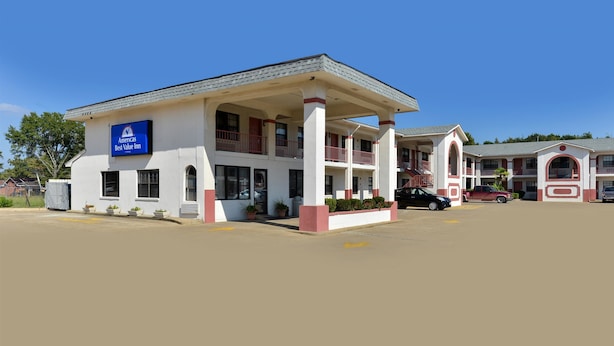 A Best Value Inn with a white facade, red accents, and a covered front area with potted plants. - Americas Best Value Inn Meridian (Meridian)