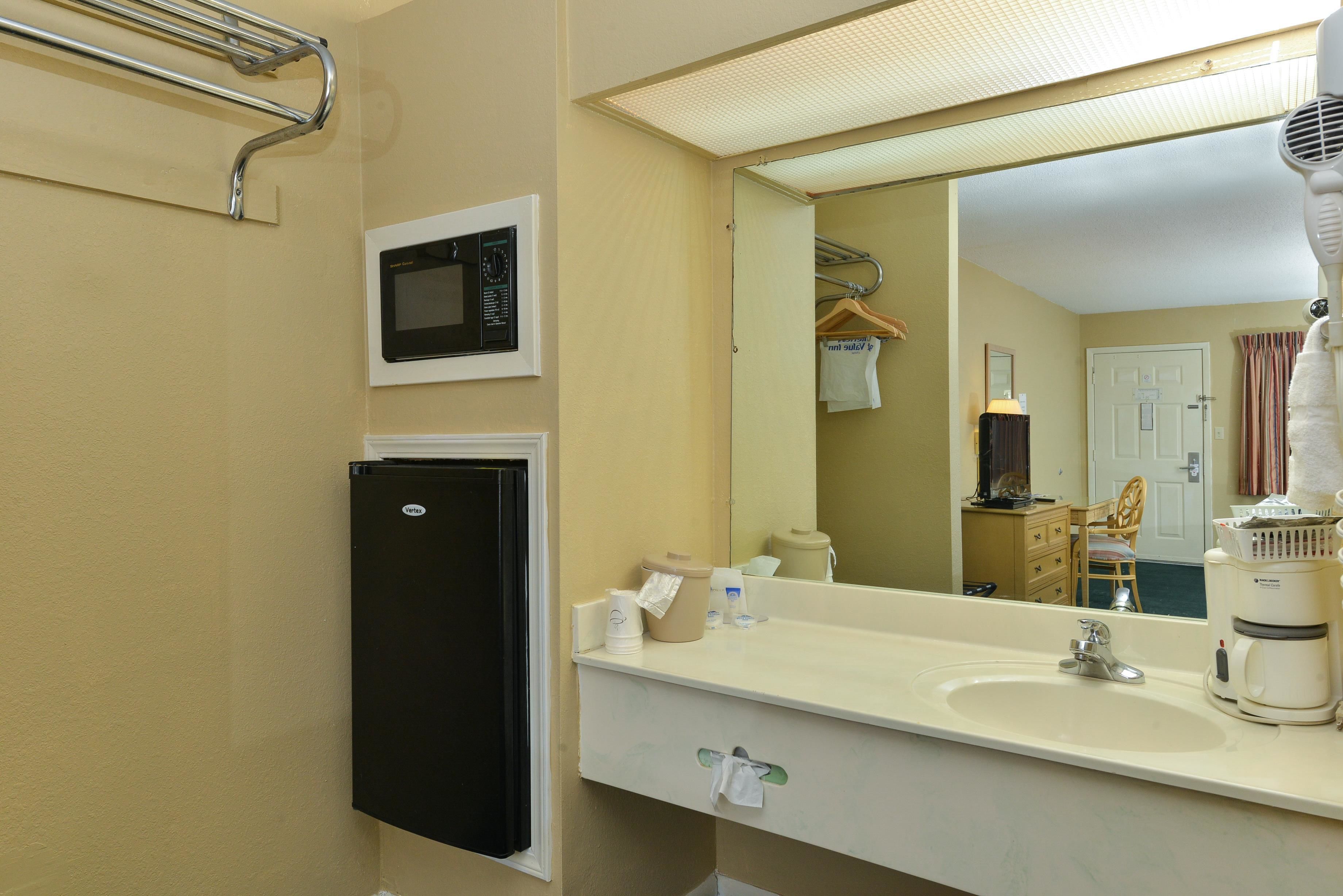 Ein Badezimmer mit Waschbecken, Spiegel, Handtuchhalter und kleinem Kühlschrank.