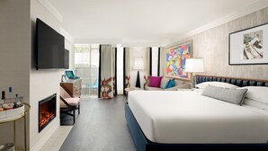 A hotel room with a large bed, a flat-screen TV, a fireplace, a sofa, a chair, and a painting on the wall.