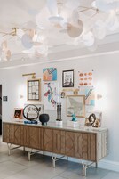 A modern interior with a glass-top console table, wall art, and a unique ceiling light fixture.