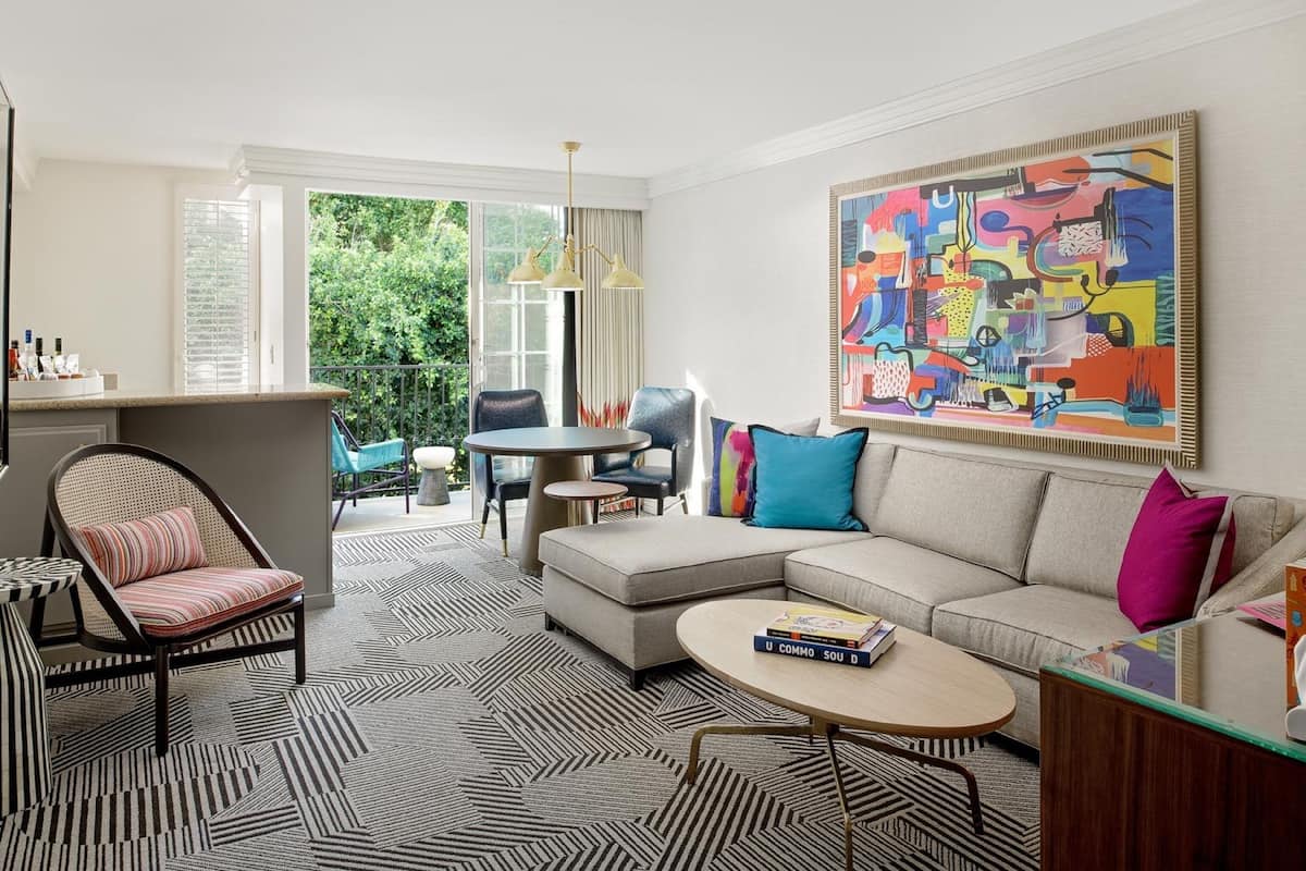 A modern living room with a sectional sofa, a round coffee table, and a striped rug. There is a dining area with a table and chairs, and a large abstract painting on the wall.