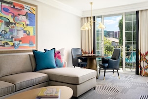 A modern living room with a sectional sofa, a round coffee table, a glass-top table with chairs, and a large abstract painting on the wall.