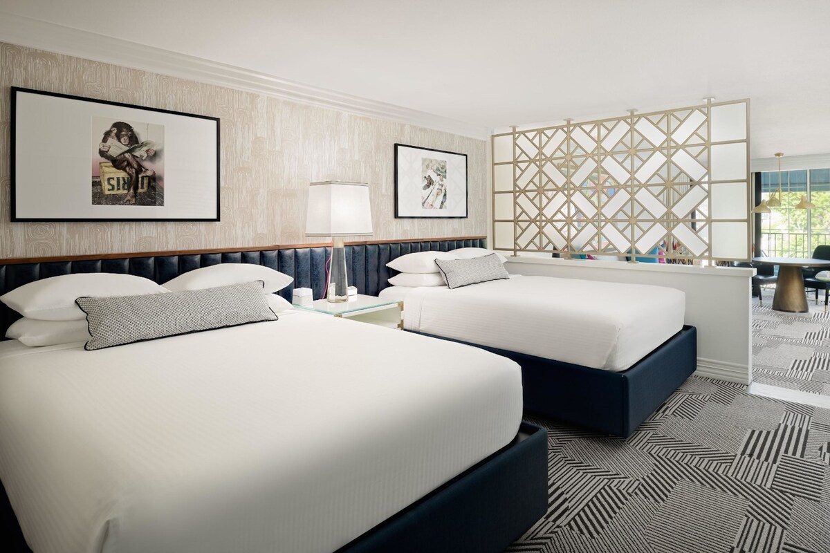 Une chambre d’hôtel avec deux lits, un bureau, une chaise, une lampe et une fenêtre donnant sur un beau paysage.