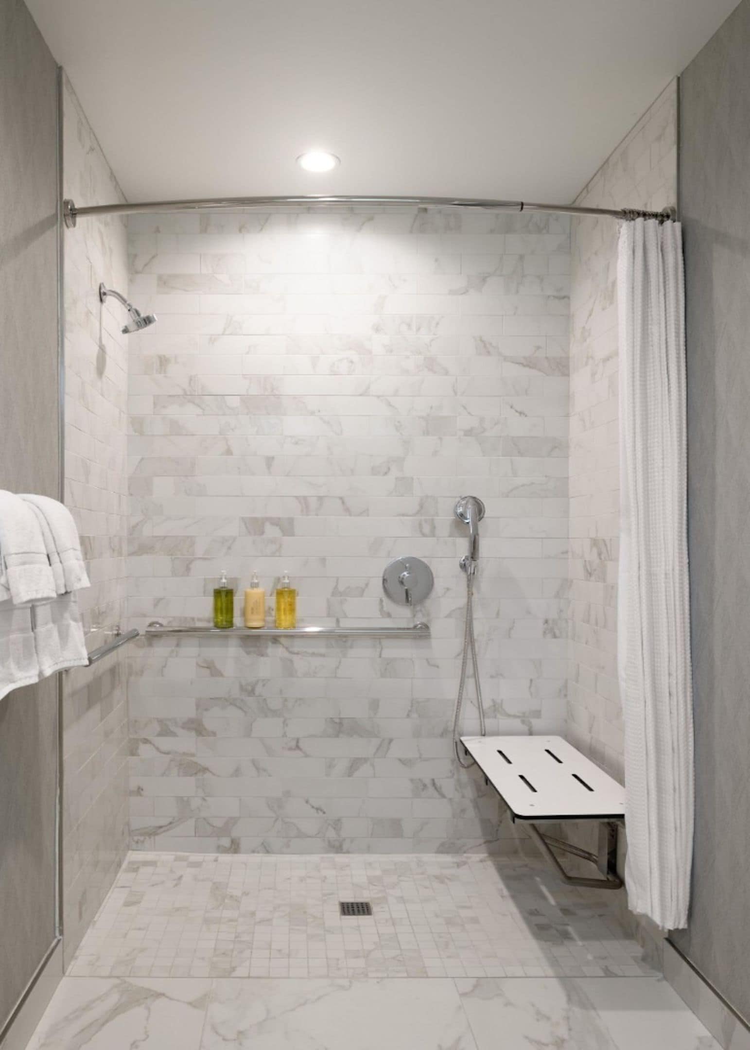 Une douche avec un mur en marbre, une étagère pour les articles de toilette et un porte-serviettes.