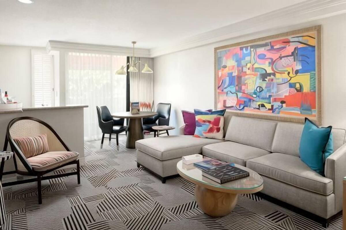 A modern living room with a sofa, armchair, coffee table, and a dining area with chairs and a table.