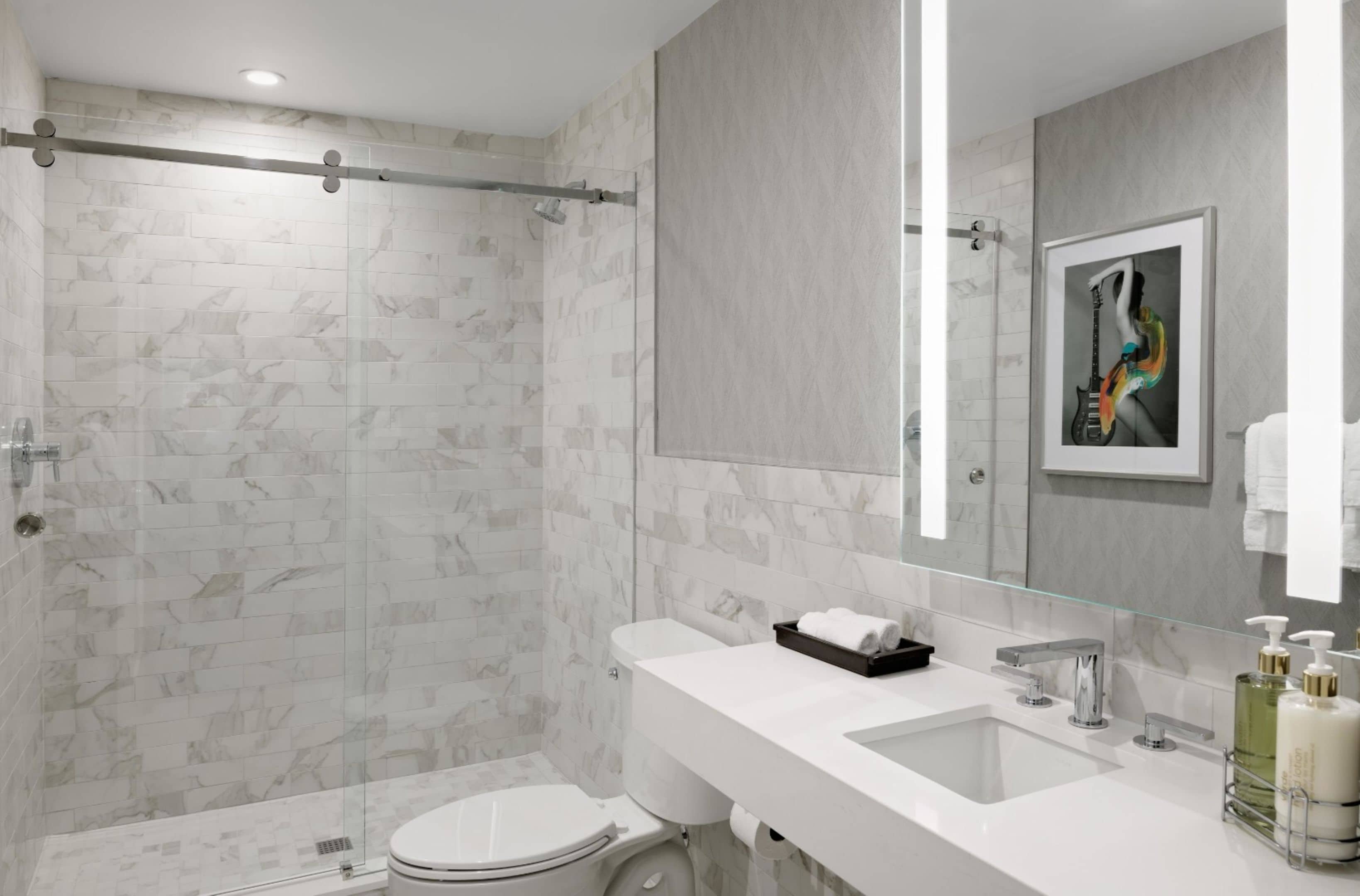 A modern bathroom with a glass shower enclosure, a white sink, and a mirror with a framed picture.