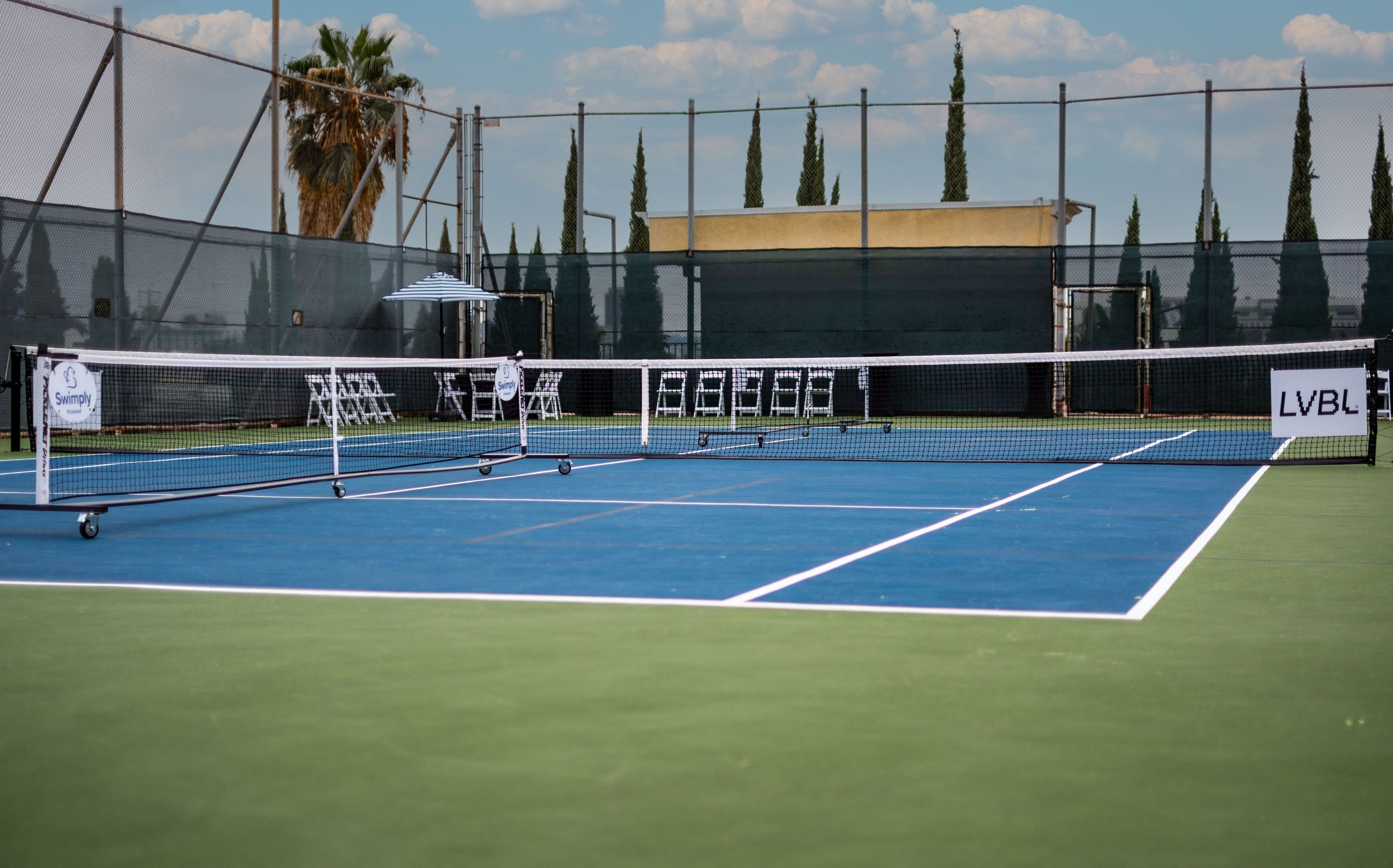 Pistes de tennis amb xarxa, envoltades per una tanca i un edifici al fons.