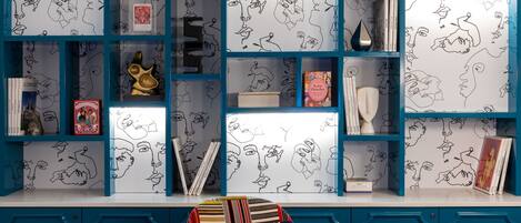 Une pièce avec un mur bleu, un tableau blanc recouvert de dessins et une étagère remplie de livres et d’objets décoratifs.