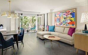 Ein modernes Wohnzimmer mit einer Couch, einem Couchtisch und Sesseln, ein Essbereich mit Tisch und Stühlen und ein Balkon mit Blick auf Bäume.