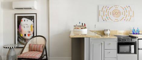 A kitchen with a microwave, stove, and sink. There is a chair and a table with a decorative item on the wall.