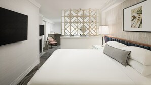 A hotel room with a large bed, a TV mounted on the wall, a desk with a lamp, and a decorative screen.