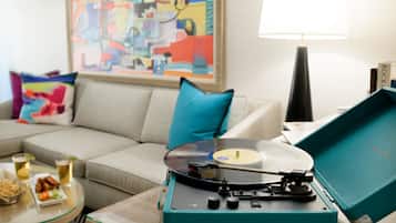 A living room with a teal record player, a beige sofa, a colorful abstract painting, and a lamp.