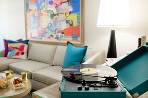 A living room with a teal record player, a beige sofa, a colorful abstract painting, and a lamp.