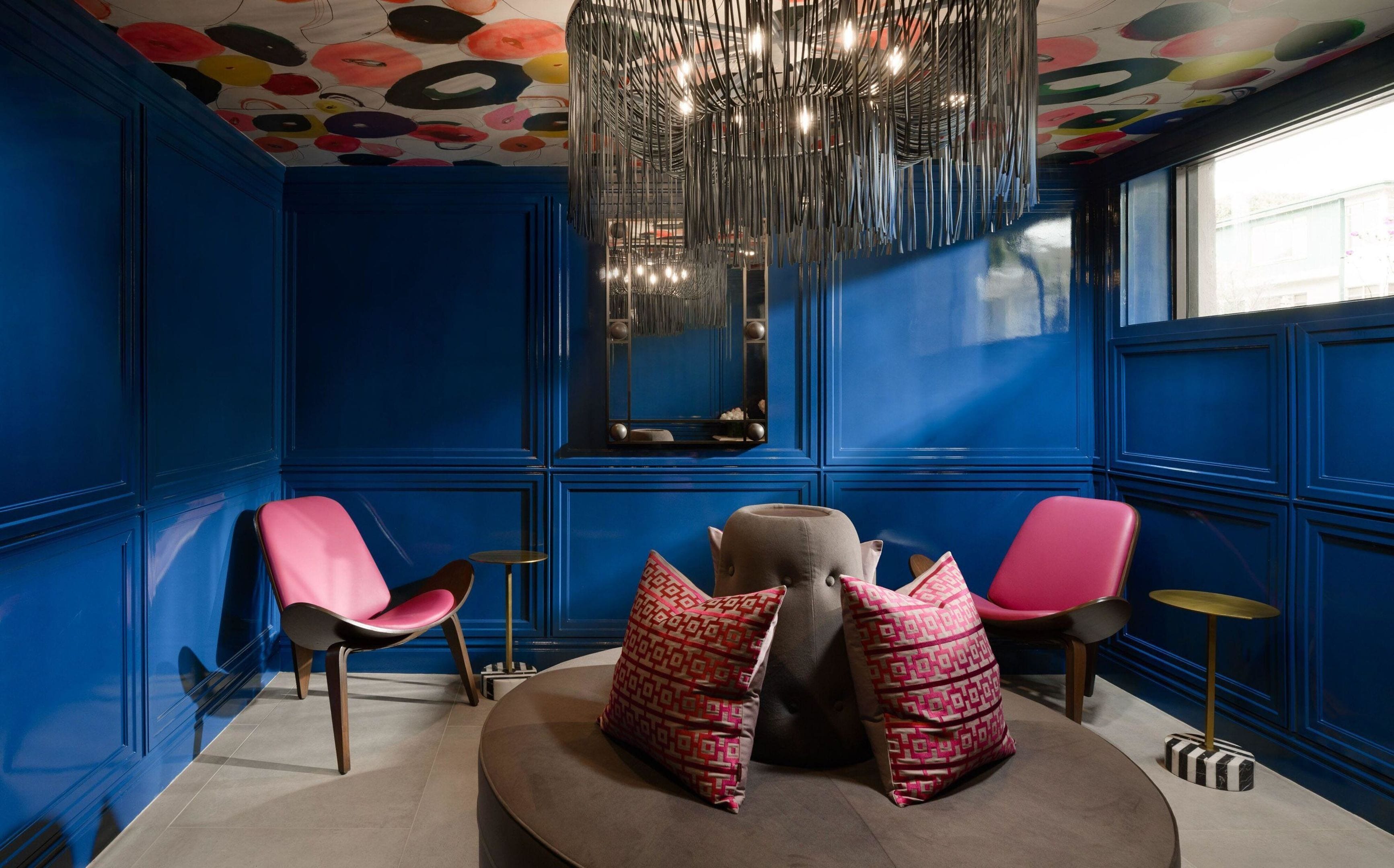 A room with blue walls, a round table, two chairs, a mirror, and a ceiling with a colorful pattern.