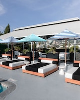 Un área de lounge en la azotea con varias camas tipo lounge, sombrillas a rayas y una piscina.
