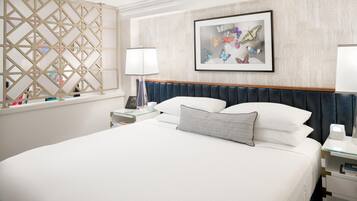 A hotel room with a large bed, a bedside table with a lamp, a nightstand with a phone, and a wall-mounted artwork.
