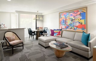 A modern living room with a sectional sofa, a round coffee table, a dining area with a table and chairs, and a large abstract painting on the wall.