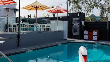 A swimming pool with a swan float, umbrellas, and a lifeguard sign.