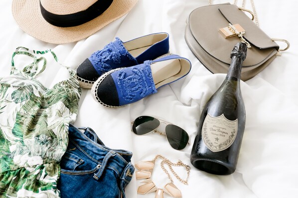 A bed with a straw hat, blue lace slippers, a grey handbag, a bottle of champagne, sunglasses, a floral print bikini, and denim shorts. -  Le Parc at Melrose (West Hollywood)