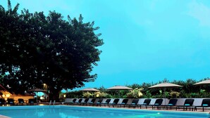 A swimming pool with lounge chairs and umbrellas, surrounded by trees and a building with lights. - Sheraton Lagos Hotel (Lagos)